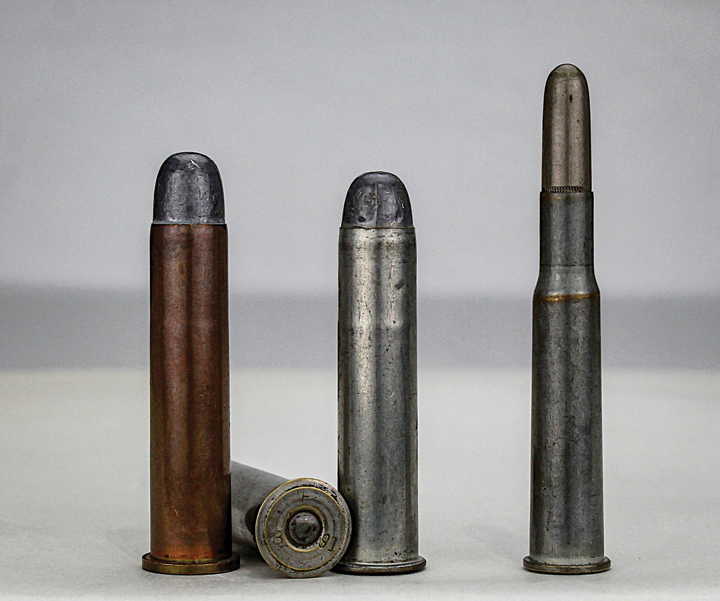 A copper-case 45-70 Government Carbine cartridge (left) stands with two examples of “tinned” cases – one shows an 1891 headstamp (center). A 30-40 Krag (right) is also tinned. All were manufactured at Frankford Arsenal.